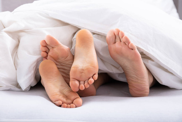 Close-up Of Couple's Bare Feet Under White Blanket - Foto, afbeelding