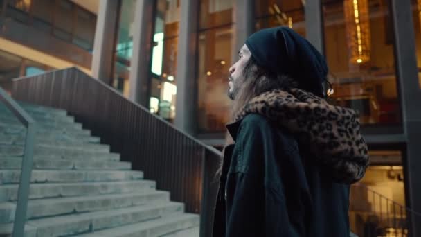 Portré hosszú hajú hipster séta az utcán a modern városban - Felvétel, videó
