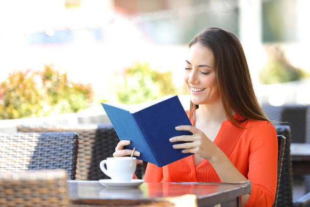 Happy woman relaxing reading a book sitting in a coffee shop terrace - Foto, imagen