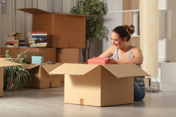 Happy woman moving home unboxing belongings sitting on the floor in the night - Foto, Bild
