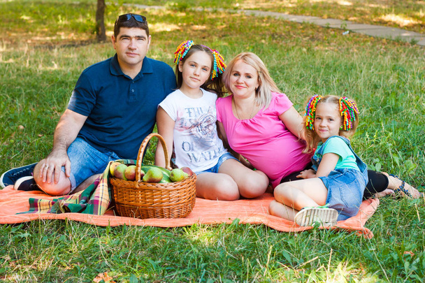 Heureuse famille à deux parents avec deux filles sur une couverture de pique-nique orange dans le parc
 - Photo, image