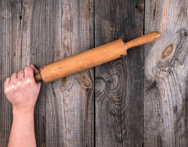 female hands hold old wooden rolling pin on a wooden table, top view - Foto, Imagen