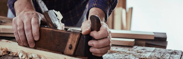 Panorama banner of a carpenter planing wood using an old-fashioned wooden plane on a rustic workbench in a close up on his hands - Fotoğraf, Görsel