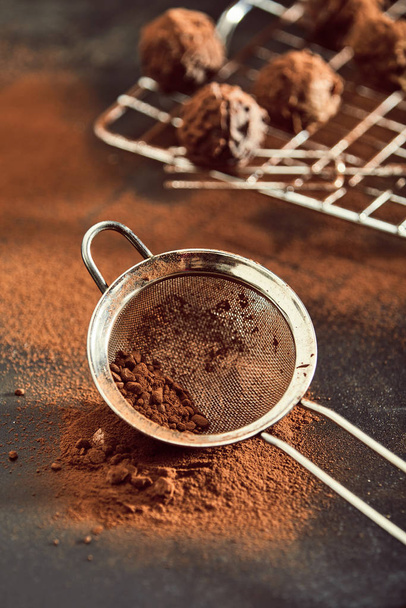 Cooking or baking with chocolate concept with bonbons or chocolate balls cooling on a wire rack and sieve with scattered powder in the foreground on a rustic wood table - Photo, image
