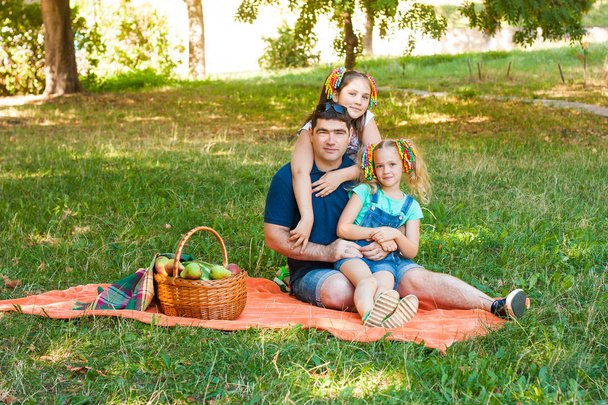 Onnellinen isä, jolla on kaksi tytärtä Oranssilla eväsretkellä puistossa
 - Valokuva, kuva