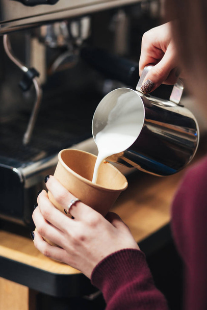 Barista kávét készít. Tejet öntenek az üvegből egy csésze kávéba, a kávét pedig egy barista készíti. Koncentrálj a kezedre egy csésze kávét tartva. - Fotó, kép