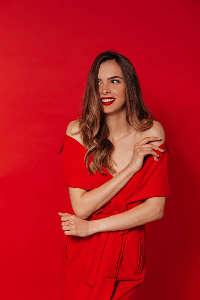 Sonriente mujer feliz en vestido rojo con labios rojos posando sobre fondo rojo en el estudio
.  - Foto, imagen