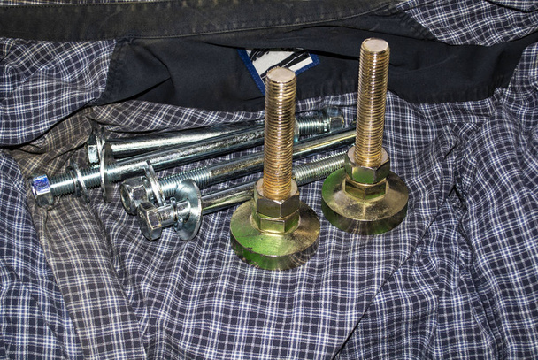 Śruby z nakrętkami i podkładkami leżące na starej koszuli w kratkę - Zdjęcie, obraz
