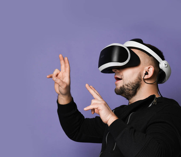 Young bearded man wearing virtual reality glasses pointing fingers up. Smartphone using with VR goggles - Фото, зображення