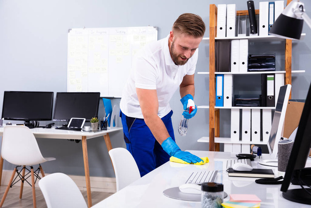 Janitor cleaning white desk in modern office - Fotó, kép