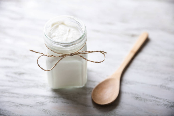 An Opened Jar With Yogurt Near Wooden Spoon On Wooden Table - Фото, изображение
