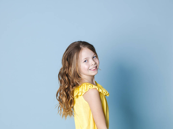 jolie fille avec des cheveux bruns avec haut jaune pose devant fond bleu
 - Photo, image