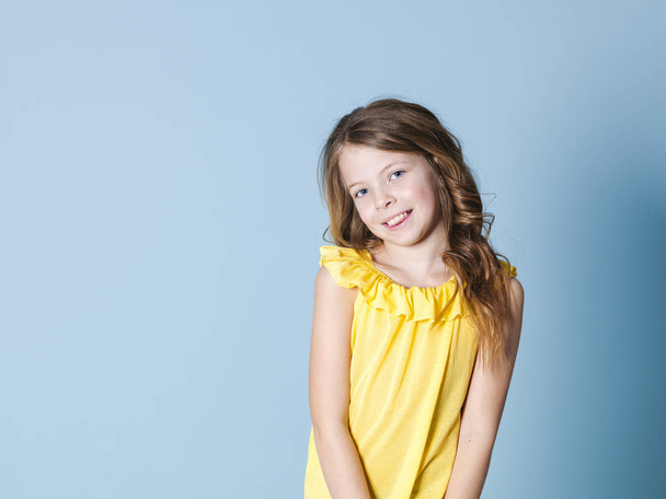 pretty girl with brunette hair with yellow top is posing in front of blue background - Φωτογραφία, εικόνα