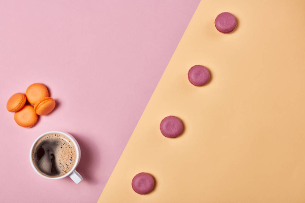 Still life with cup of coffee and delicious macaroons lying on background consisting of two colores pink and yellow. Top view with copy space. Design element for menu of cafe - Фото, зображення