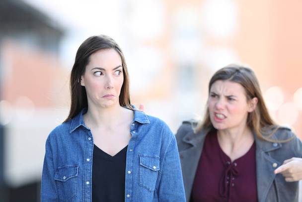 Front view portrait of an angry woman scolding her confused friend in the street - Photo, image