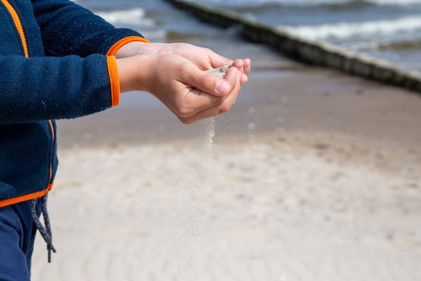 a little boy slowly lets sand flow through his hands scattered by the wind. - Photo, image