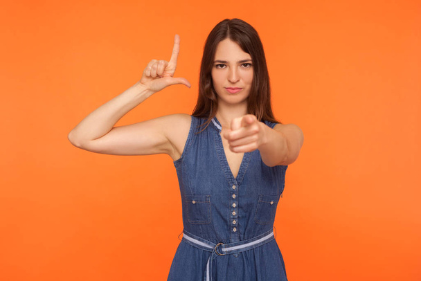Bossy woman in denim dress showing L sign and pointing to camera - Фото, изображение