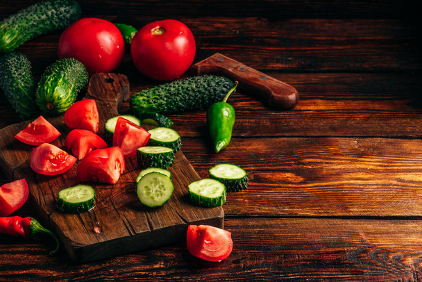 Sliced vegetables. Tomatoes, cucumbers and chili peppers over wooden background. - 写真・画像