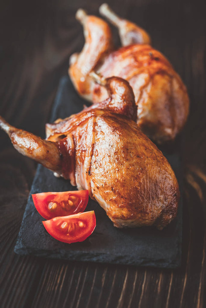 Two baked quails wrapped in bacon on the black stone board - Photo, image