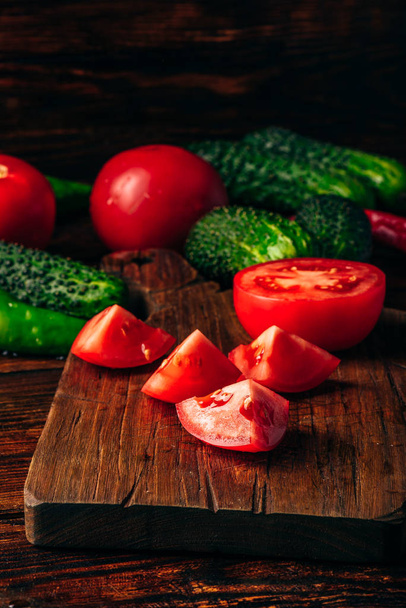Sliced tomatoes on cutting board and cucumbers with chili peppers over wooden background. - Φωτογραφία, εικόνα