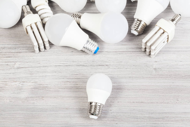 top view of white LED bulb light and several energy-saving lamps on gray wooden board - 写真・画像