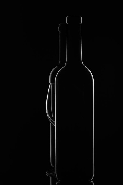 Silhouette of two wine bottles and empty wineglass on a black background with reflection.  Contour with gradient and highlights - 写真・画像