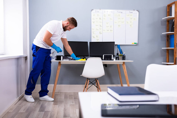 Janitor cleaning white desk in modern office - Foto, afbeelding
