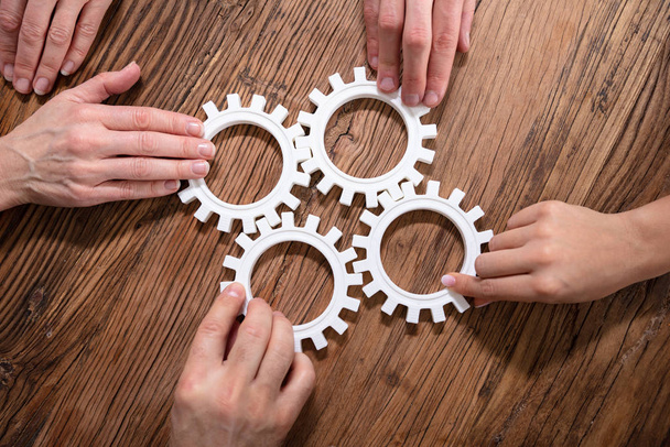 Group Of Businesspeople Joining Together Gears On Wooden Table At Workplace - 写真・画像