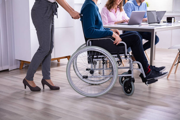 Smiling Young Businesswoman Helping Disabled Colleague In Wheelchair - Foto, Bild