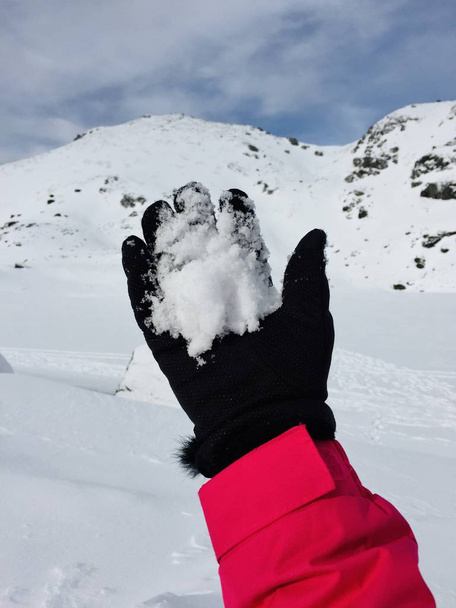 Χέρι κρατώντας χιόνι φορούν μαύρα γάντια ροζ σακάκι χιόνι καλύπτονται τοπίο βουνό χειμώνα κρύο εποχή τυχοδιώκτης - Φωτογραφία, εικόνα