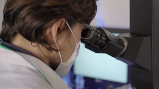 Scientist in a laboratory uses a microscope. Closeup shot - Felvétel, videó