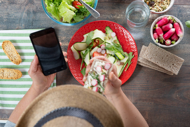 woman eating a vegan salad and using a smartphone, top view - Foto, Imagen
