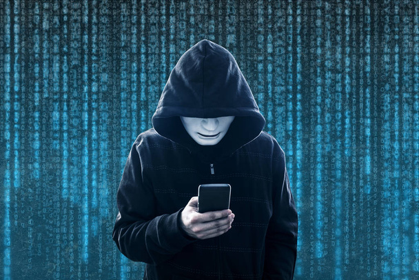 Hooded hacker with mask holding smartphone - Foto, Imagem