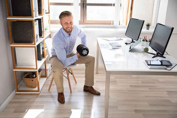 Attractive Businessman Exercising With Dumbbells In Office - Fotografie, Obrázek