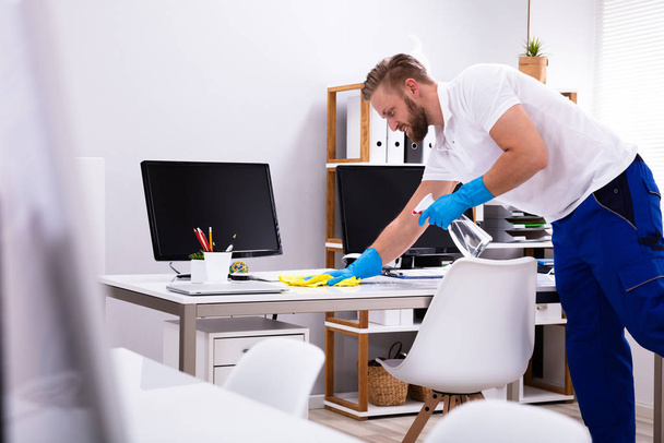 Janitor cleaning white desk in modern office - Foto, afbeelding
