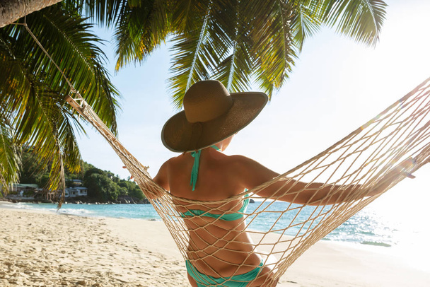 Rear View Of Young Woman In Bikini And Hat Sitting On Hammock On The Beach - Fotoğraf, Görsel