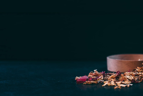 Chá espalhado pétalas de rosa com um pote de madeira em um fundo escuro
 - Foto, Imagem