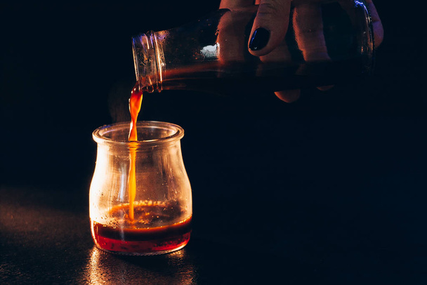Coffee is poured into a glass jar with milk on a dark background with warm light - Foto, Imagem
