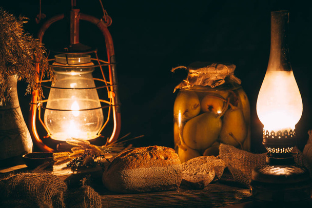 Homemade baked bread on a wooden board in warm light from gas lamps. Rustic vintage surroundings - Photo, Image