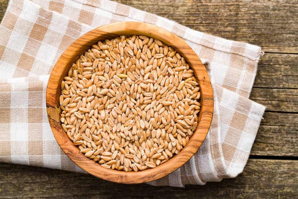 Healthy spelt grains in wooden bowl. - Foto, imagen