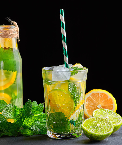 refreshing drink lemonade with lemons, mint leaves, ice cubes and lime in a glass on a black background, copy space - Zdjęcie, obraz