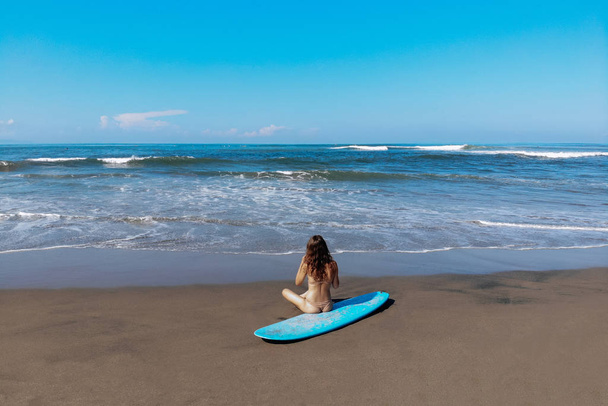 beautiful sporty surfing woman in sexy bikini sit on longboard surf surfboard board on beach before surfing. Modern active sport lifestyle and summer vacation - Fotó, kép