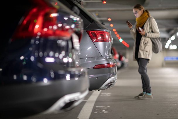 Underground garage or modern car parking with lots of vehicles, perspective of the row of the cars with a female driver looking for her vehicle - Photo, image