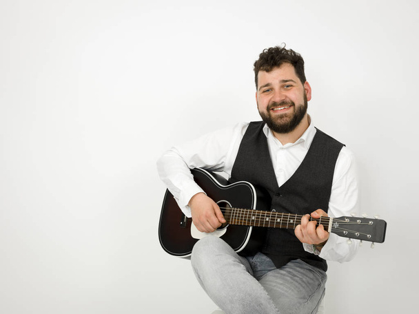 man with black hair and beard playing and singing with acoustic guitar on white background - Foto, imagen