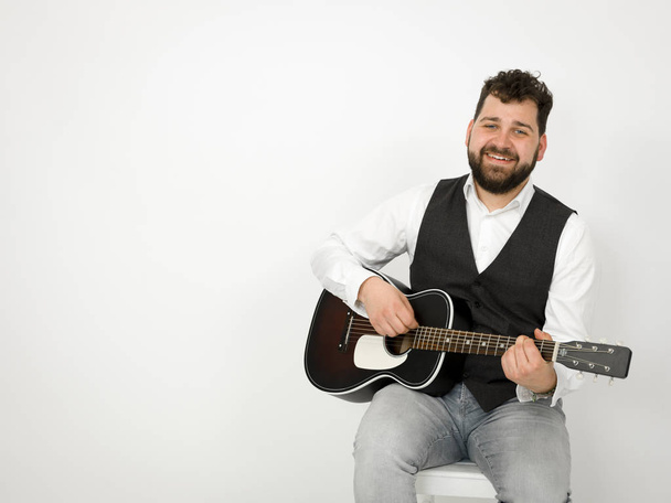 man with black hair and beard playing and singing with acoustic guitar on white background - Foto, Imagen