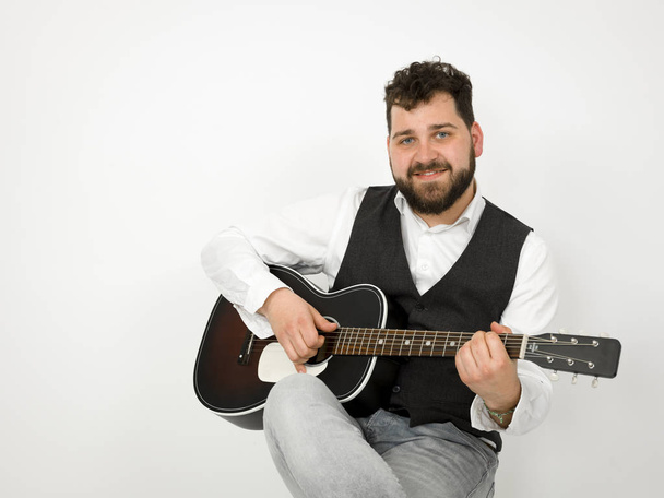 man with black hair and beard playing and singing with acoustic guitar on white background - Foto, Imagen
