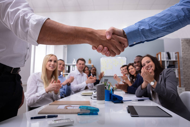 Two Male Professionals Shaking Hands With Team Sitting By Clapping Hands After A Successful Meeting - Foto, imagen