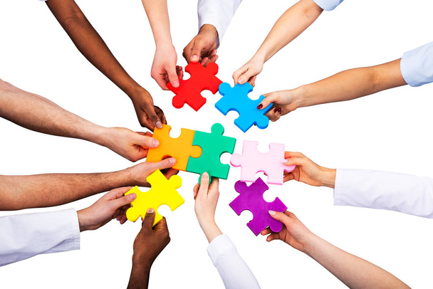 High Angle View Of Medical Team Solving Colorful Jigsaw Puzzle Against White Background - Photo, image