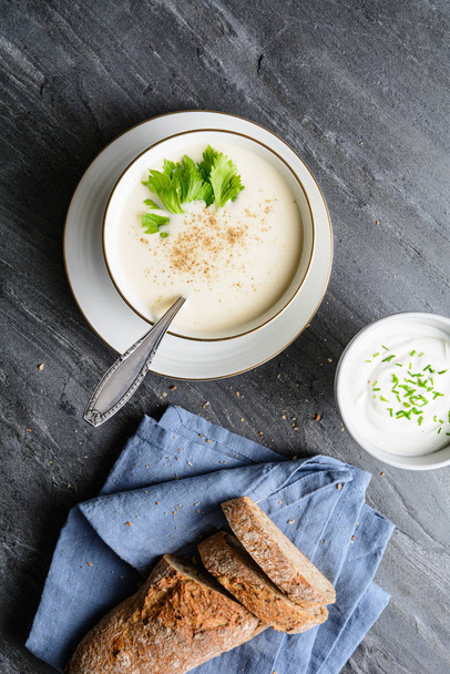 Delicious creamy celery soup topped with black pepper and fresh leaves, served with crusty bread - Photo, Image