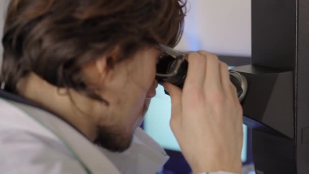 Scientist in a laboratory uses a microscope. Closeup shot - Metraje, vídeo